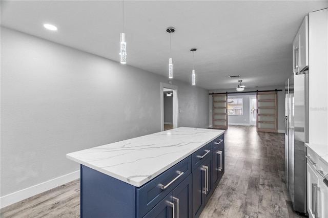 kitchen with blue cabinetry, white cabinetry, stainless steel refrigerator, pendant lighting, and a barn door