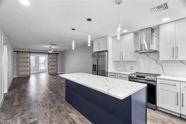 kitchen with wall chimney range hood, stainless steel appliances, a center island, white cabinets, and a barn door