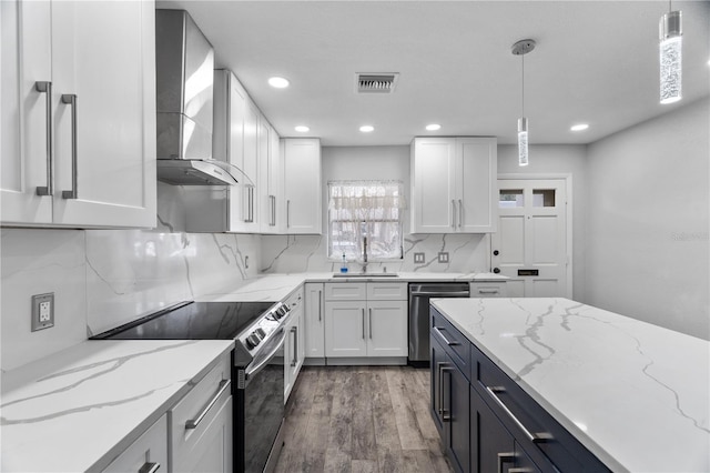 kitchen featuring wall chimney exhaust hood, sink, hanging light fixtures, appliances with stainless steel finishes, and white cabinets