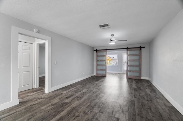 empty room with dark hardwood / wood-style floors, a textured ceiling, a barn door, and ceiling fan