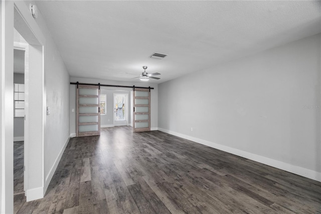 unfurnished living room with a textured ceiling, dark wood-type flooring, a barn door, and ceiling fan