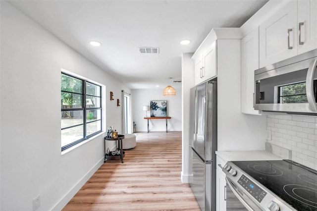 kitchen with appliances with stainless steel finishes, backsplash, white cabinets, and light wood-type flooring