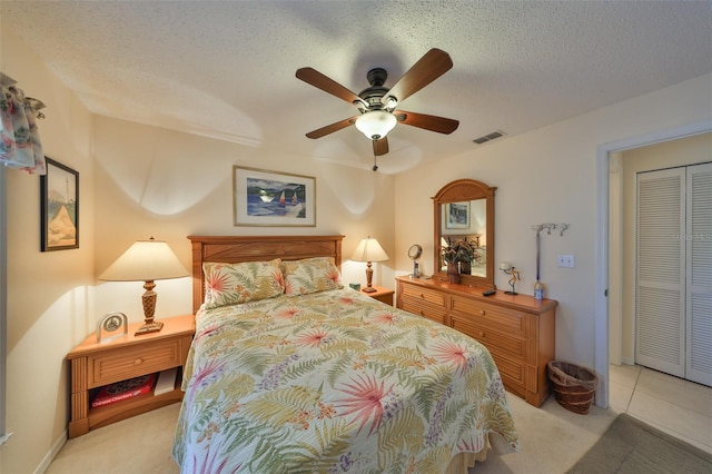 bedroom with ceiling fan, light carpet, a textured ceiling, and a closet