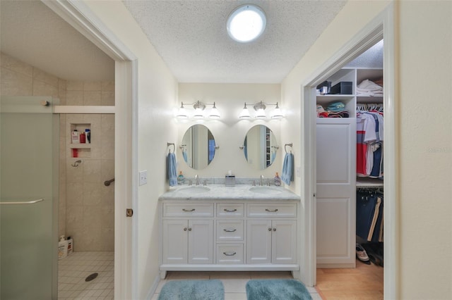 bathroom with a textured ceiling, double vanity, a stall shower, and a sink