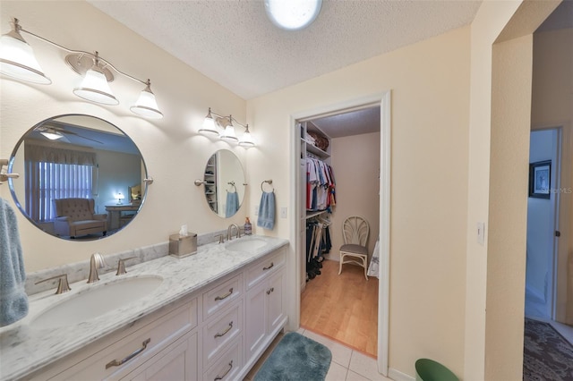 bathroom with double vanity, a textured ceiling, a sink, and tile patterned floors