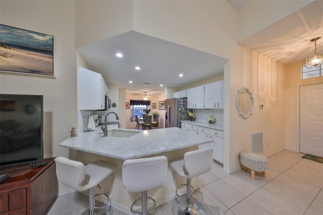 kitchen featuring light stone counters, tasteful backsplash, white cabinets, stainless steel fridge with ice dispenser, and kitchen peninsula