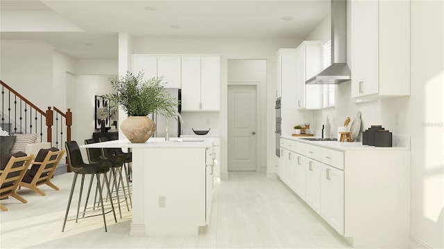 kitchen with sink, a breakfast bar area, white cabinets, a kitchen island with sink, and wall chimney exhaust hood