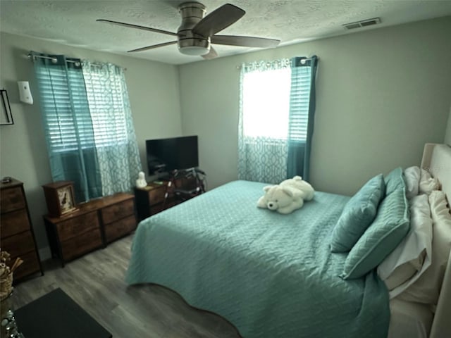 bedroom featuring ceiling fan, a textured ceiling, multiple windows, and light wood-type flooring