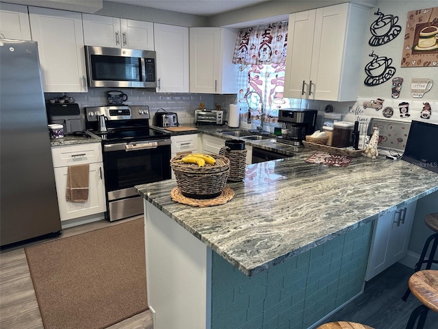 kitchen with stone counters, white cabinetry, stainless steel appliances, tasteful backsplash, and wood-type flooring