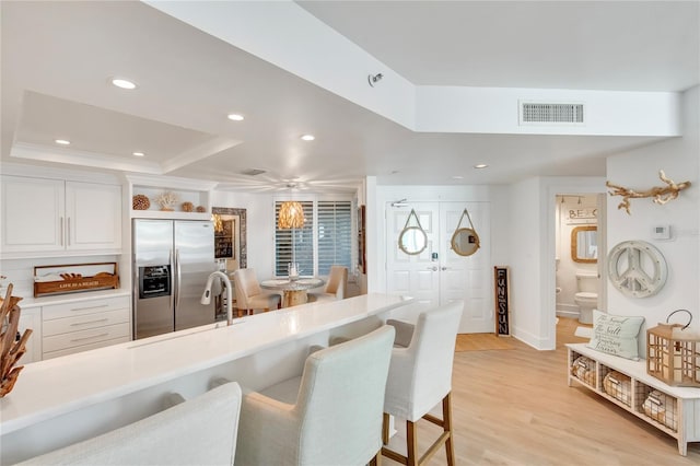 kitchen featuring built in fridge, a breakfast bar, white cabinetry, light hardwood / wood-style floors, and a tray ceiling