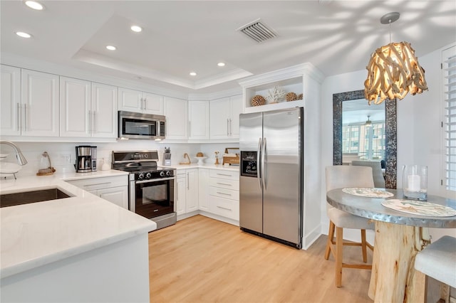 kitchen featuring a raised ceiling, sink, white cabinets, hanging light fixtures, and stainless steel appliances