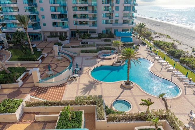 view of swimming pool featuring a view of the beach, a patio area, and a water view