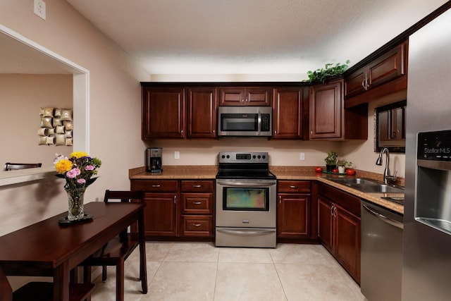 kitchen with sink, light tile patterned floors, dark brown cabinets, stainless steel appliances, and a textured ceiling