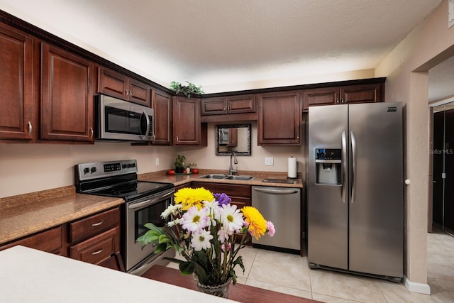 kitchen with light tile patterned flooring, sink, stainless steel appliances, dark brown cabinets, and a textured ceiling