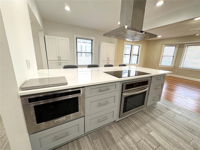 kitchen featuring gray cabinetry, wall oven, black electric stovetop, island range hood, and oven