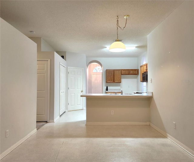 kitchen with hanging light fixtures, sink, kitchen peninsula, and a textured ceiling