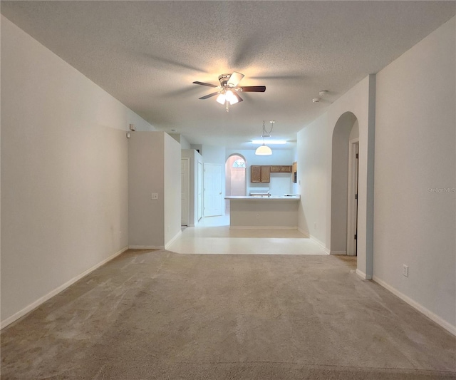 empty room with ceiling fan, light colored carpet, and a textured ceiling