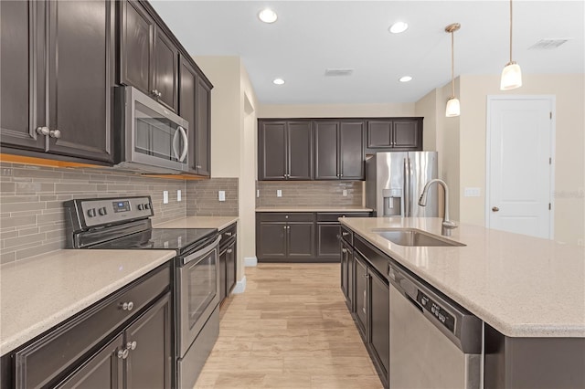 kitchen featuring pendant lighting, sink, dark brown cabinetry, stainless steel appliances, and light stone countertops