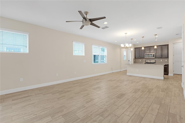 unfurnished living room featuring plenty of natural light, ceiling fan with notable chandelier, and light wood-type flooring