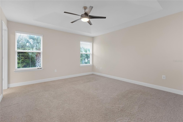 empty room featuring light carpet, a raised ceiling, and ceiling fan