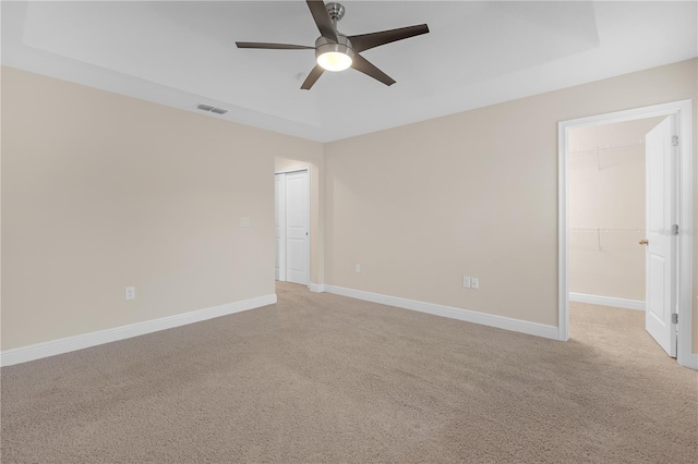 empty room with a tray ceiling, light colored carpet, and ceiling fan