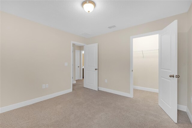 unfurnished bedroom with a spacious closet, light colored carpet, and a closet