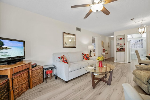 living room featuring ceiling fan with notable chandelier, a textured ceiling, and light wood-type flooring