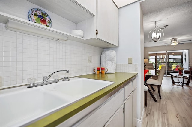 kitchen with ceiling fan with notable chandelier, sink, backsplash, white cabinets, and light wood-type flooring