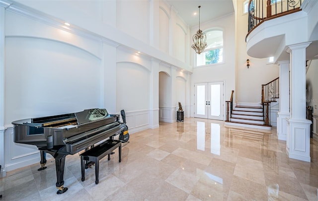 foyer with french doors, crown molding, a chandelier, a towering ceiling, and decorative columns