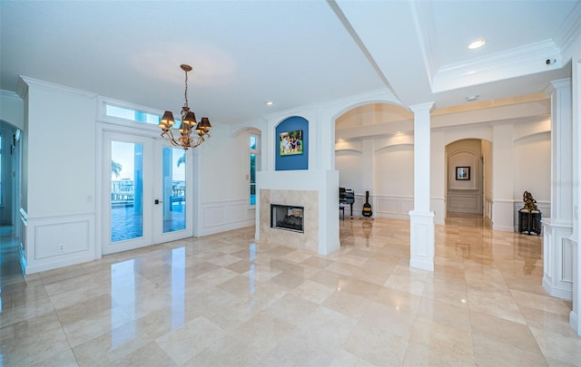 unfurnished living room with crown molding, a multi sided fireplace, a chandelier, and ornate columns