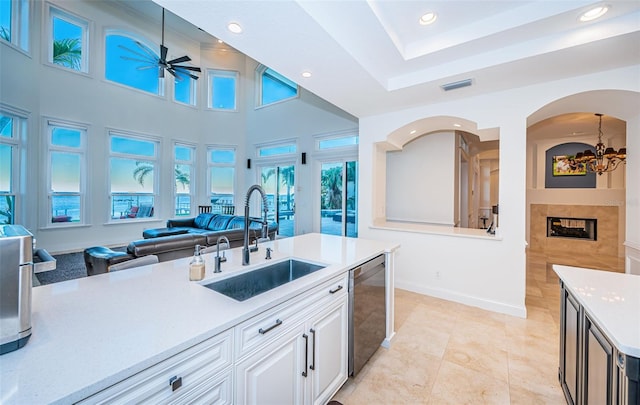 kitchen with a towering ceiling, ceiling fan with notable chandelier, sink, white cabinets, and stainless steel dishwasher