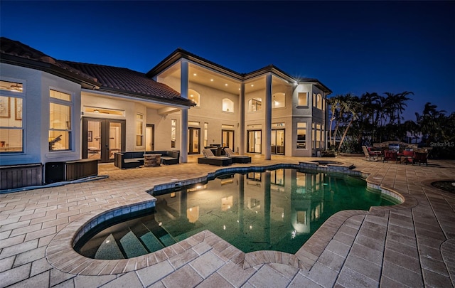 pool at night with an outdoor hangout area, a patio, and french doors