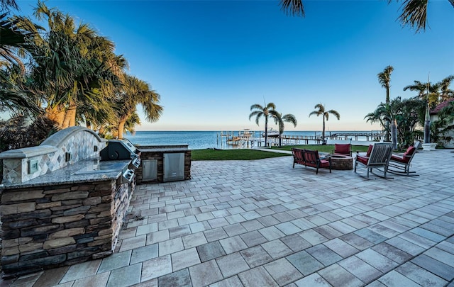 view of patio featuring a water view, area for grilling, a bar, and an outdoor fire pit