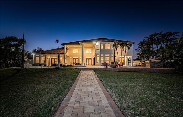 back house at night featuring a yard, a patio, and a balcony