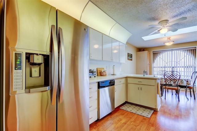 kitchen featuring appliances with stainless steel finishes, a skylight, white cabinets, kitchen peninsula, and light wood-type flooring