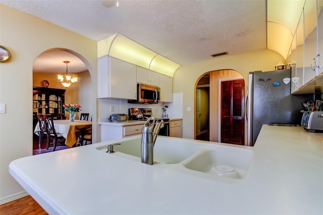 kitchen featuring a textured ceiling, kitchen peninsula, a notable chandelier, stainless steel appliances, and white cabinets