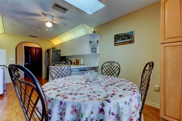 dining room featuring ceiling fan, a textured ceiling, light wood-type flooring, and a skylight