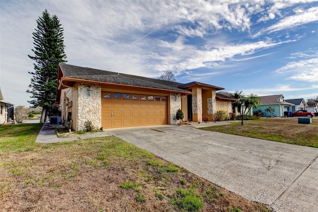 view of front facade featuring a front lawn, concrete driveway, central AC, a garage, and stone siding