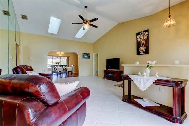tiled living area with visible vents, vaulted ceiling with skylight, a ceiling fan, and arched walkways