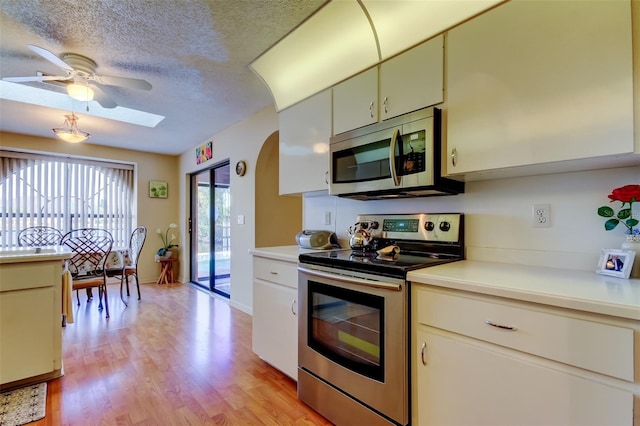 kitchen with light wood-type flooring, light countertops, appliances with stainless steel finishes, a textured ceiling, and a ceiling fan