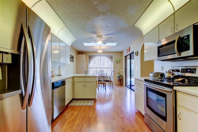 kitchen with a peninsula, light wood-style flooring, stainless steel appliances, light countertops, and a textured ceiling