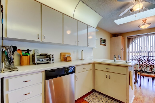 kitchen featuring a textured ceiling, stainless steel dishwasher, a peninsula, a skylight, and light countertops