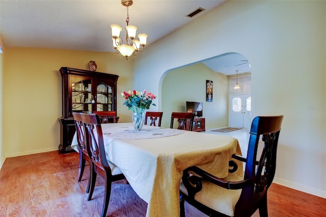 dining room with visible vents, a notable chandelier, wood finished floors, arched walkways, and baseboards