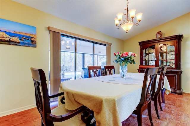 dining room with light wood-style flooring, lofted ceiling, baseboards, and a chandelier