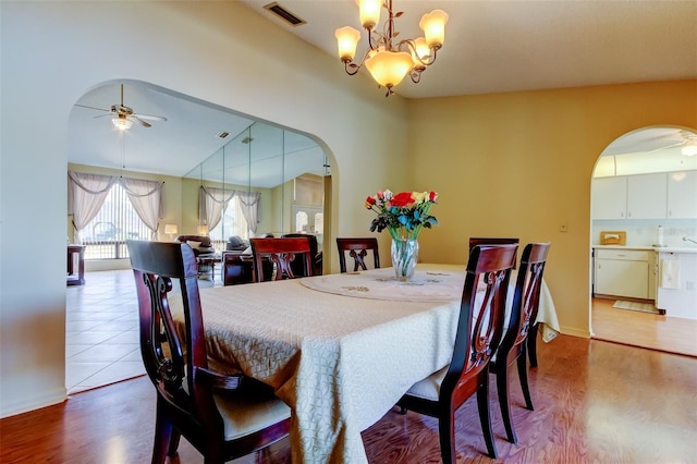 dining space with arched walkways, visible vents, ceiling fan with notable chandelier, and wood finished floors