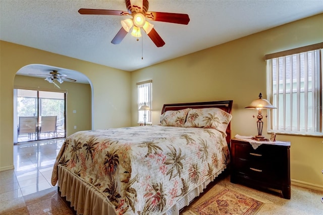 bedroom featuring multiple windows, arched walkways, a textured ceiling, and access to exterior