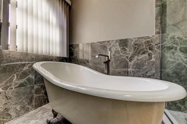full bath with tile walls, a freestanding bath, and marble finish floor