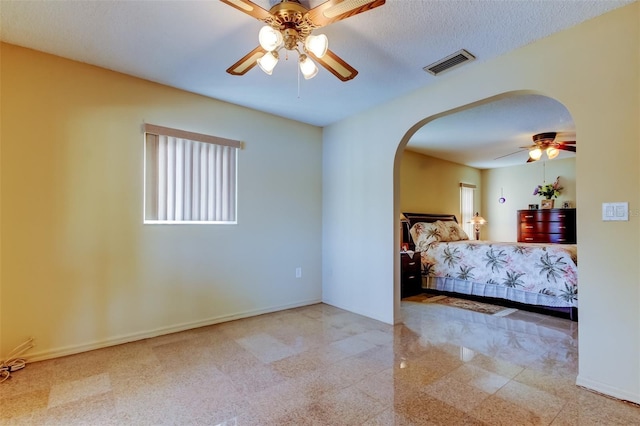 unfurnished bedroom featuring visible vents, baseboards, arched walkways, ceiling fan, and a textured ceiling