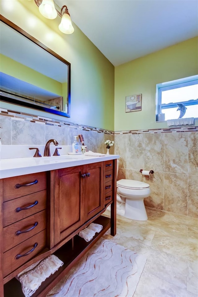 bathroom with wainscoting, toilet, vanity, and tile walls
