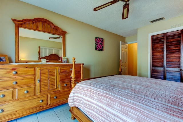 bedroom with a ceiling fan, visible vents, light tile patterned flooring, a closet, and a textured ceiling